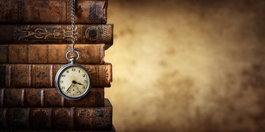 Vintage clock hanging on a chain on the background of old books. Old watch as a symbol of passing time. Concept on the theme of history, nostalgia, old age. Retro style.
