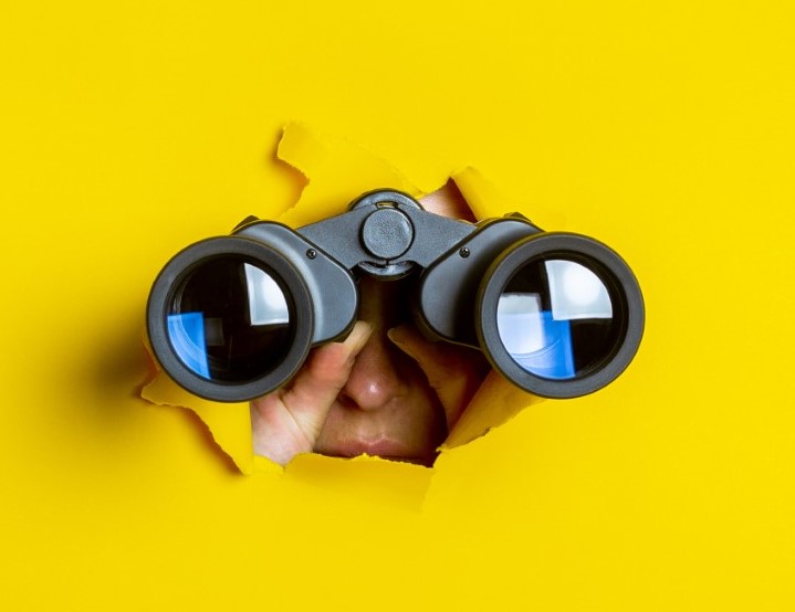 Female hand holds black binoculars on a yellow background. Journey, find and search concept. Banner