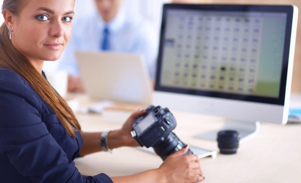 Female photographer sitting at a desk with a Mac computer and lots of picture folders showing.